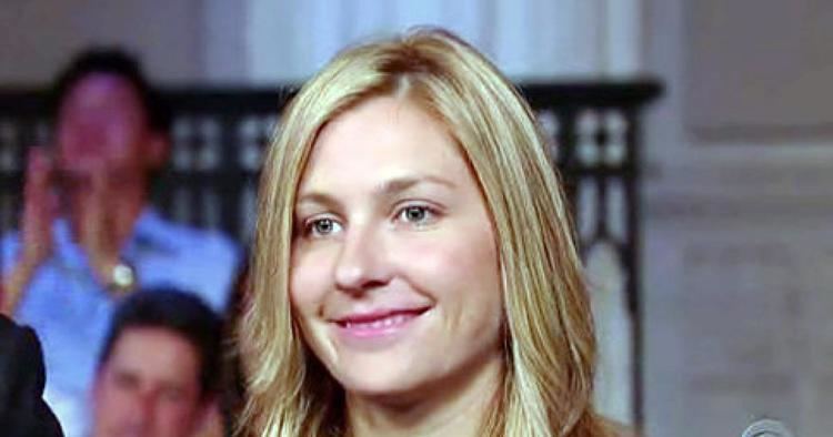 Stephanie Birkitt, smiling while looking afar, an American attorney. She has blonde wavy hair and people behind her.