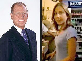 David Letterman and Stephanie Birkitt are smiling (from left to right). David with white hair is wearing eyeglasses, a violet polka dot necktie, a white collared shirt, and a pinstriped suit. Stephanie with short blonde wavy hair is wearing a gray blouse.