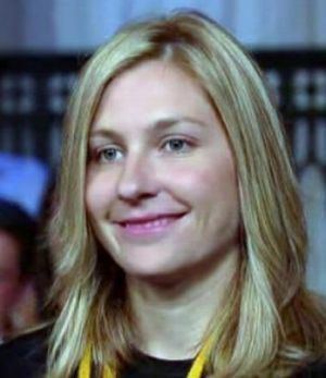 Stephanie Birkitt, smiling while looking afar, an American attorney. She has blonde wavy hair with a yellow strap over her neck, wearing a black shirt.