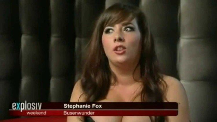 Stephanie Fox talking in an interview and wearing a strapless black dress.