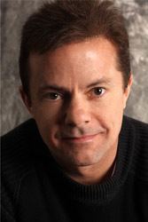 Stephen Geoffreys with a tight-lipped smile while wearing a black t-shirt