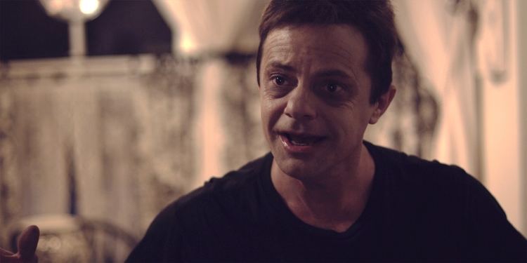 Stephen Geoffreys talking to someone while wearing a black t-shirt in a scene from the 2010 film, Mr. Hush