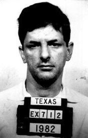 Stephen Morin's mugshot while holding a board with words and numbers written on it like "TEXAS", "EX712", and "1982". Stephen with a serious face and mustache is wearing a polo shirt