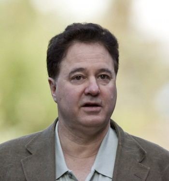 Stephen Pagliuca looking at something with a serious face and his mouth is open while wearing a gray long sleeve under a beige coat