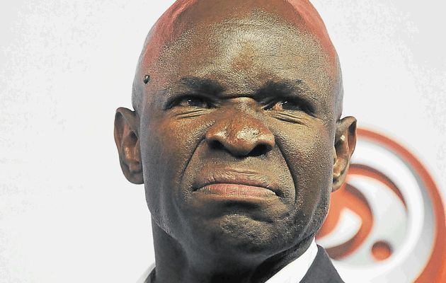 Steve Komphela with an angry face and wearing a black coat over white long sleeves.