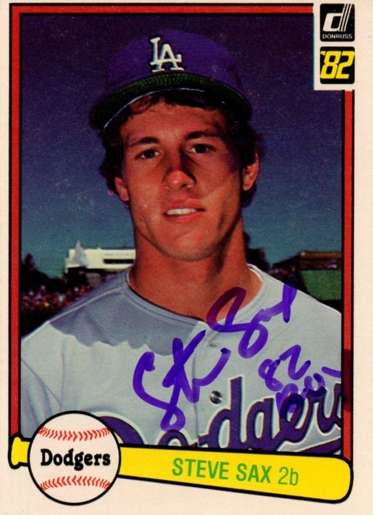 Steve Sax smiling on an autographed 1982 Donruss #624 Rookie Card dodgers with his signature on the right below of the photograph, and a ball on the left below named “dodgers” and a yellow bat named “Steve Sax 2b) besides on it. Steve has black hair wearing a blue cap with “LA” on it and a white jersey