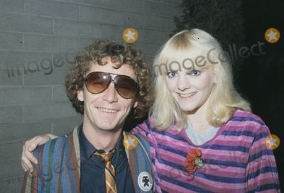 Steve Tracy smiling, with curly hair and wearing sunglasses together with his on-screen wife Alison Arngrim with a smiling face, blonde hair, and wearing a striped purple shirt.