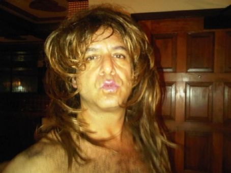 Steven G. Kaplan pouting his lips and wearing a brown shaggy wig while being topless