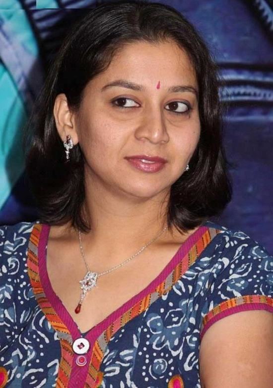 Sudha Rani wearing a blue printed shirt, a necklace, and pair of earrings