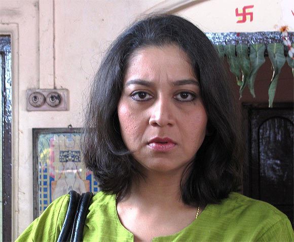 Sudha Rani wearing a green shirt while carrying a shoulder bag inside a room