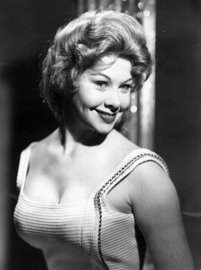 Sue Ane Langdon smiling with short wavy hair while wearing a sleeveless blouse that exposes her cleavage