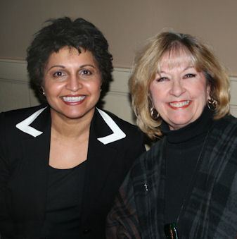 Suhana Meharchand smiling while wearing a black coat and black inner top and the woman beside her wearing black blouse