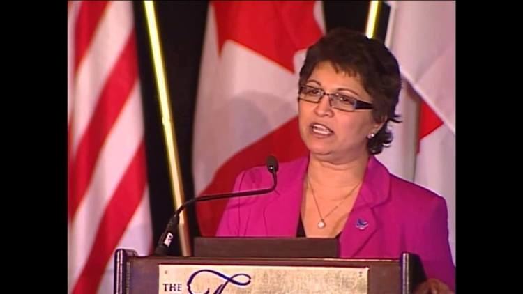 Suhana Meharchand delivering a speech while wearing a pink blazer and eyeglasses