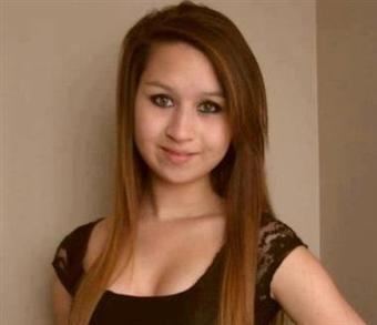 Amanda Todd with a tight-lipped smile and golden brown straight hair while wearing a black lace blouse exposing light cleavage