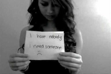Amanda Todd holding a paper with a note, "I have nobody, I need someone", with a sad face and curly hair while wearing a sleeveless blouse