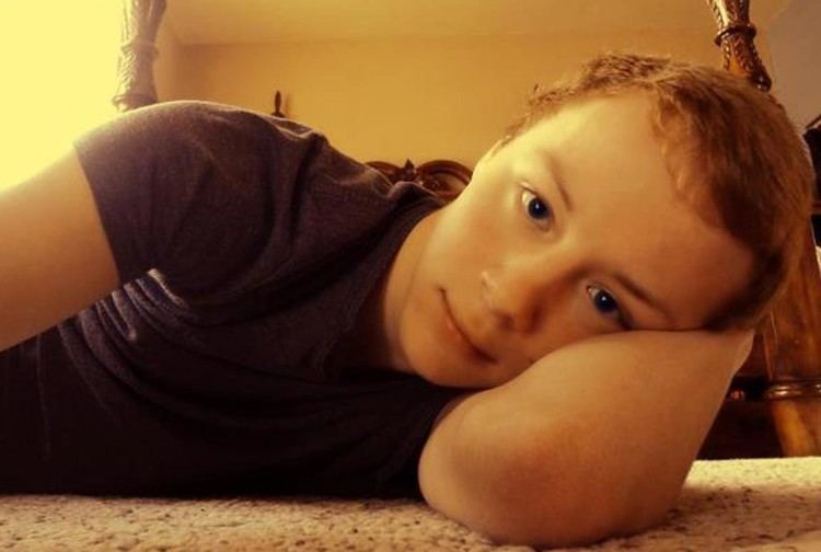 The innocent face of Jadin Bell, lying on the floor with one arm on his head and wearing a black shirt.