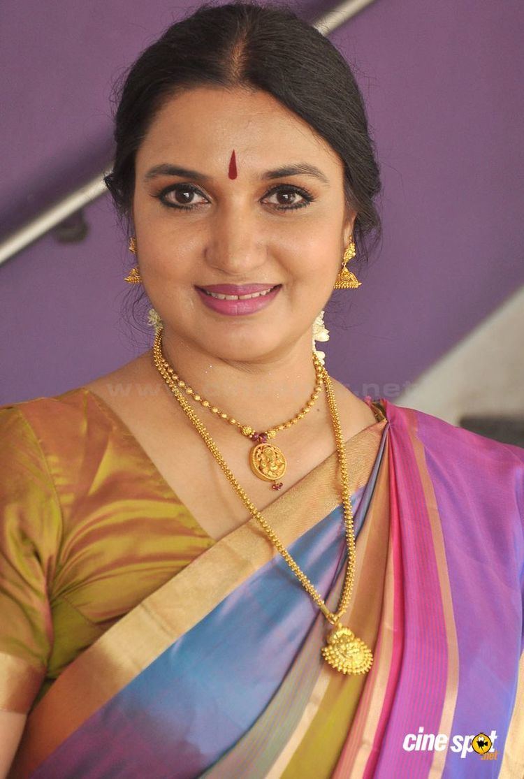 Sukanya wearing gold earrings, a gold necklace, and a colorful dress.