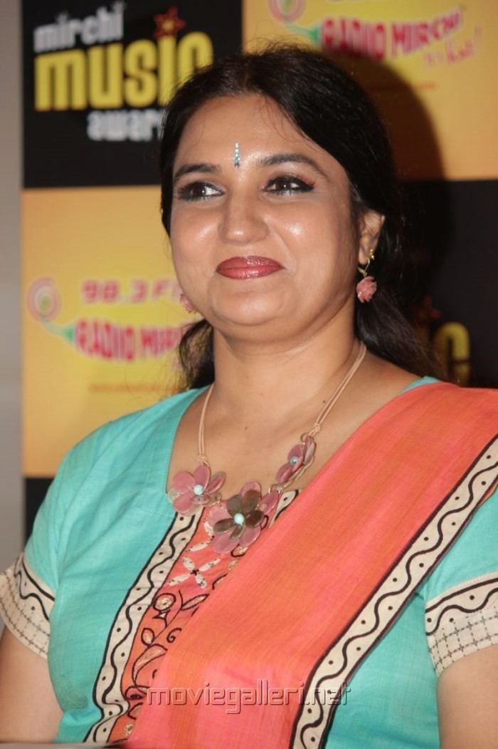 Sukanya wearing earrings, a necklace, and a color blue and orange dress.