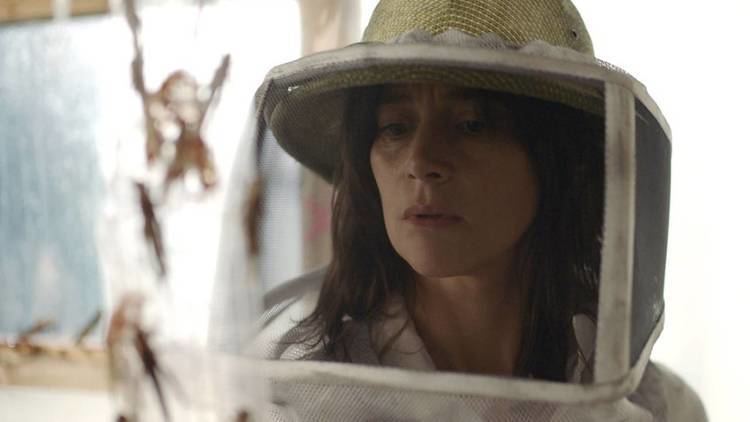 Suliane Brahim as Virginie Hébrard with a sad face and wearing a hat with protection in a movie scene from The Swarm (2020 film).