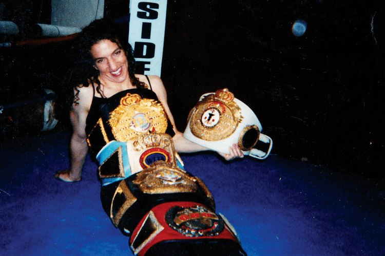 Sumya Anani smiles while holding her championship belts