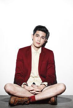 Sunny Suwanmethanon smiling and sitting down and wearing a red suit over a white shirt along with brown shoes and red socks.