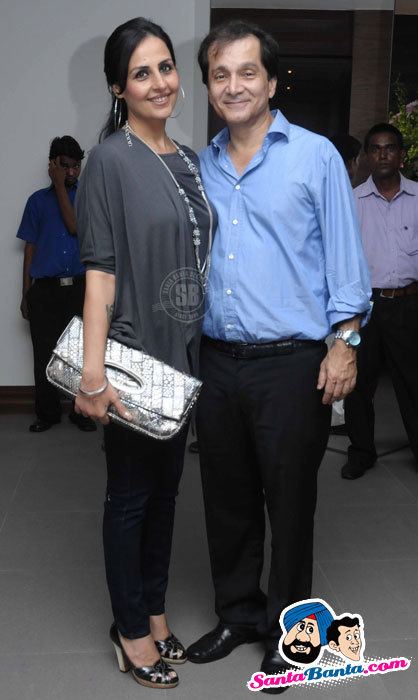 Alka Bhatia and Surendra Hiranandani are smiling. Alka wearing loop earrings, a necklace, a gray blouse, and black pants while Surendra wearing blue long sleeves and black pants.