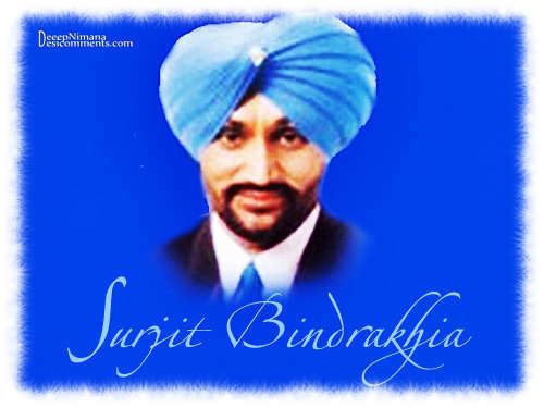 Surjit Bindrakhia smiling with a mustache and beard and wearing a white sleeve, black suit, blue necktie, and blue turban in a blue background