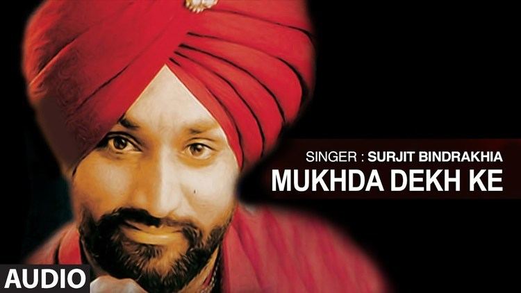 Surjit Bindrakhia smiling with a mustache and beard and wearing a red shirt and red turban in his youtube cover photo