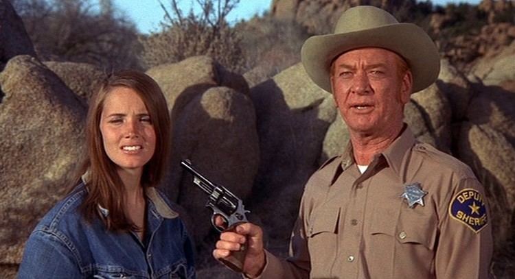 Kenneth Tobey holding a gun and pointing at Susan Foster's head in a scene from the 1971 Western action drama independent film, Billy Jack