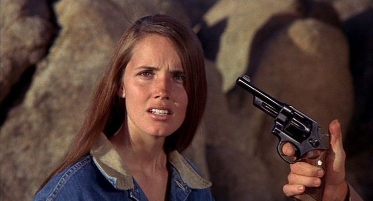 Susan Foster with a gun pointed at her head while she is wearing a denim jacket in a scene from the 1971 film, Billy Jack