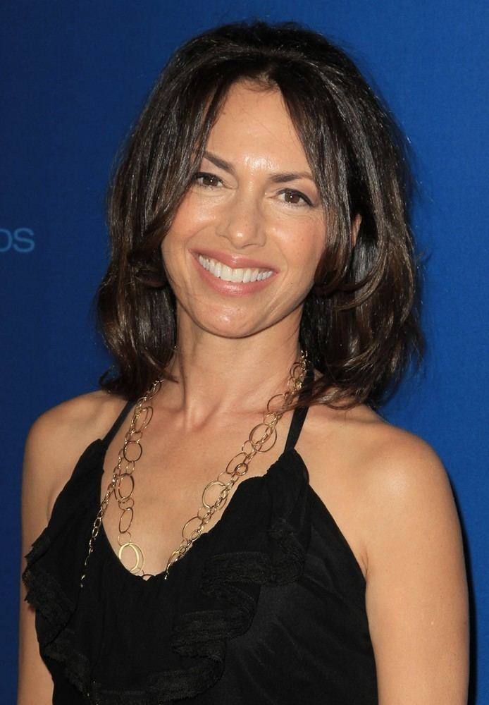 Susanna Hoffs smiling, with shoulder-length hair, wearing a chain necklace and a black halter top.