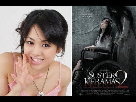 On the left is Sola Aoi, is smiling with her hand open and has black long hair tied up wearing a flower-shaped necklace and pink noodle strap top. On the right is The advertisement poster for the movie Suster Keramas 2 (2001), Sola Aoi (left) is anxious looking up with bandages over her head while sitting on a wheelchair, has long black hair wearing white long sleeve polo with blood over her shoulders and black skirt. A female ghost (right) looking at Sola Aoi while holding the wheelchair has long black hair and is wearing a long white dress.