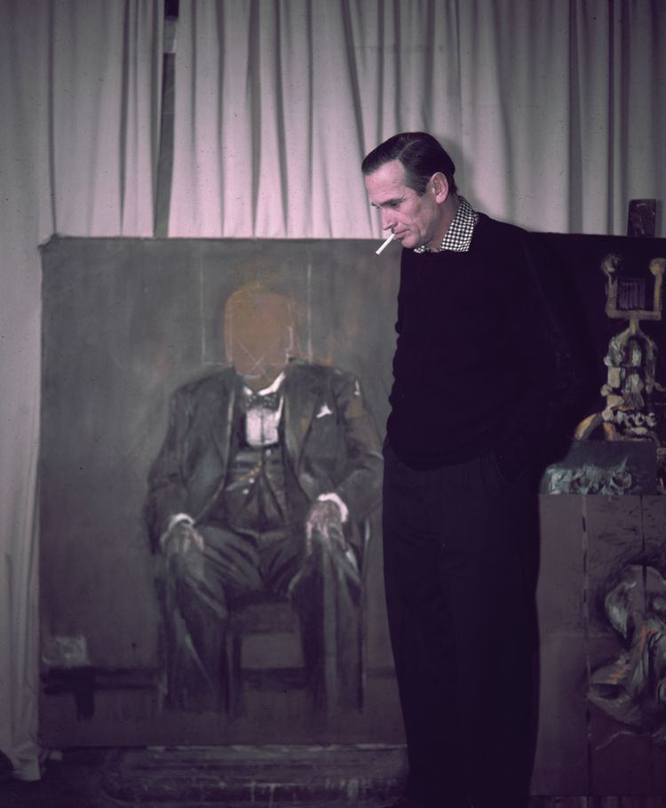 English modernist painter Graham Vivian Sutherland smoking while standing beside his unfinished portrait of Winston Churchill, 1954