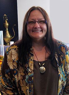 Suzan Shown Harjo wearing eyeglasses, necklace, brown inner top and brown and cream floral coat with touch of color blue