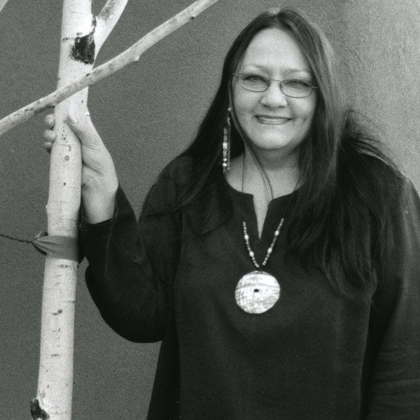 Suzan Shown Harjo wearing long sleeves, necklace and eyeglasses while holding on a branch of tree