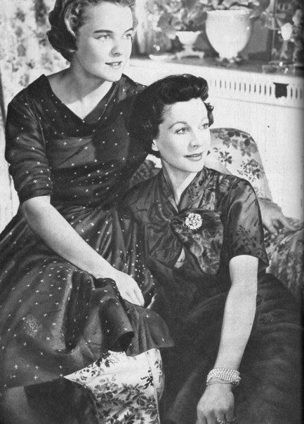 Suzanne Farrington and Vivien Leigh with serious faces while looking at something and sitting on a couch. Both are with short hair and wear black dresses.