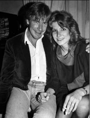 James Hunt smiling and wearing a coat and long sleeves and beside him is Sarah Lomax smiling while holding a cigarette and wearing a blouse