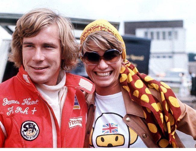 James Hunt smiling and wearing a red jacket beside him is Suzy Miller with a big smile while wearing a polka dot bandana and sunglasses