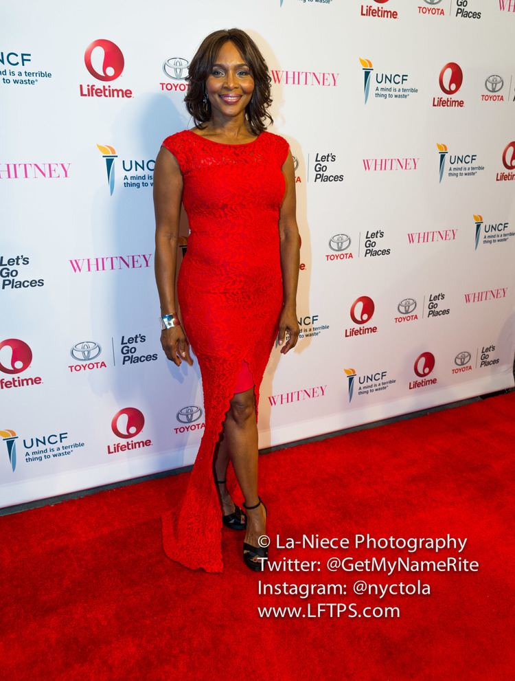 Suzzanne Douglas smiling while wearing a red dress and black heels