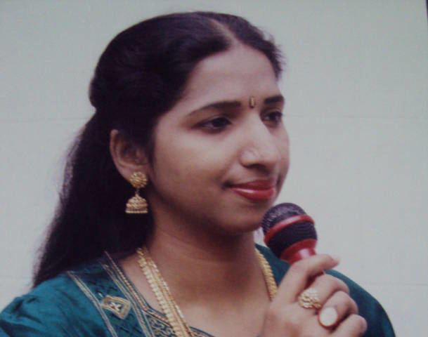 Swarnalatha wearing blue dress and gold jewelries while holding a microphone