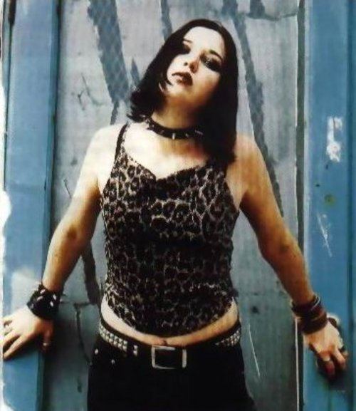 Talena Atfield posing on a wall wearing a black leopard sleeveless shirt, a belt, and some accessories