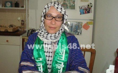 Tali Fahima with a tight-lipped smile while wearing a black and white hijab, blue blouse, eyeglasses, and green sash