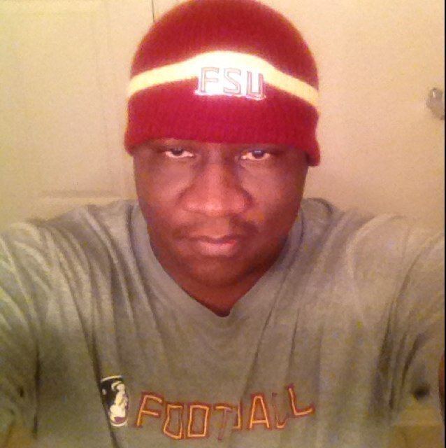 Tamarick Vanover looking serious while wearing a gray shirt and a red and yellow bonnet