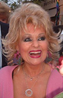 Tammy Faye Messner with a big smile while wearing necklaces and pink dress