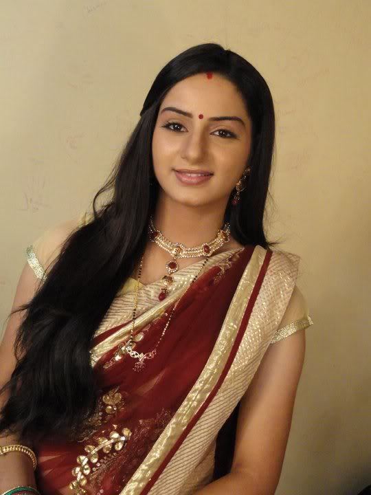Tanvi Bhatia smiling, with long black hair, wearing earrings, a necklace, and a yellow and red Indian dress.