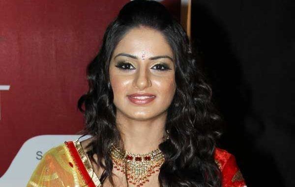 Tanvi Bhatia smiling, with curly long hair, wearing a necklace, and a red and yellow Indian dress.