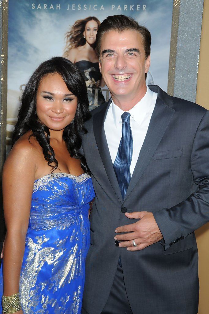 Tara Lynn Wilson smiling and wearing blue dress while Chris Noth laughing and wearing coat, white long sleeves and blue neck tie