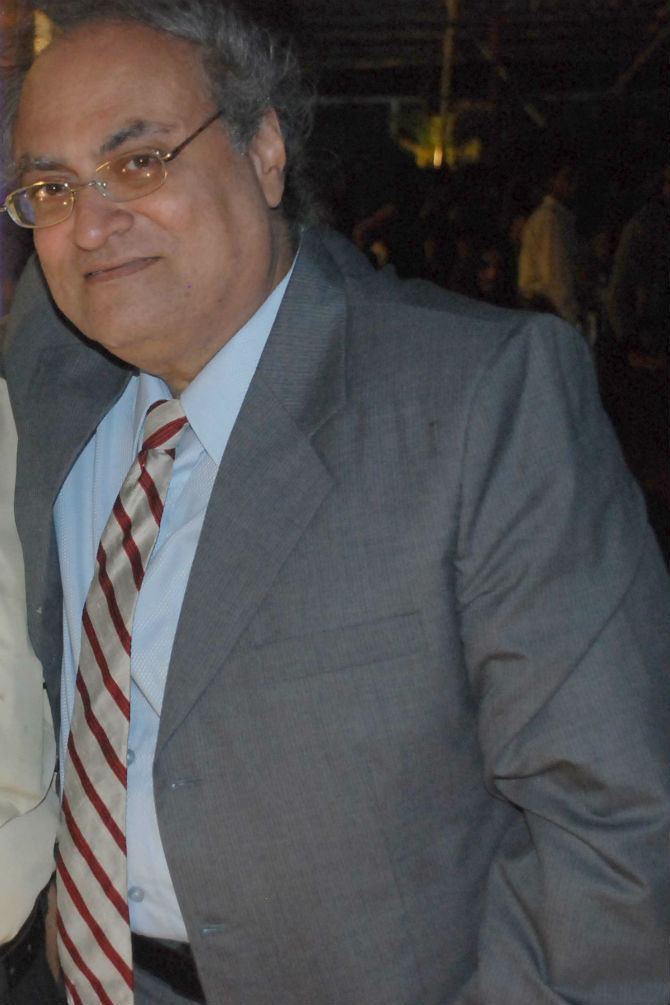 Tariq Khan (actor) smiles while wearing a blue shirt, a gray coat, and a tie