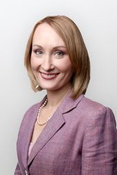 Tasha Kheiriddin smiling, with short blonde hair, wearing pearl necklace and a purple blazer.
