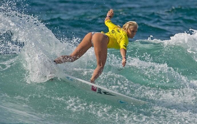 Tatiana Weston-Webb surfing while wearing a yellow t-shirt and bikini